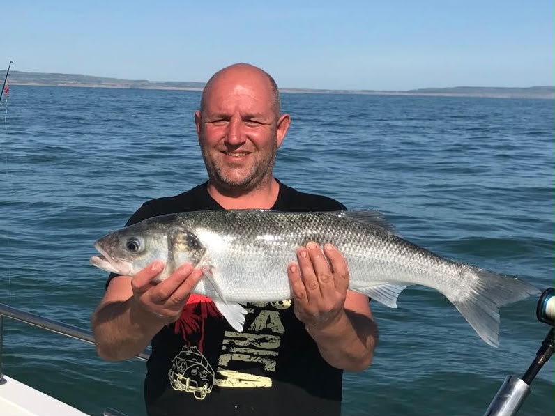 Angler holding a silver fish with the sea behind