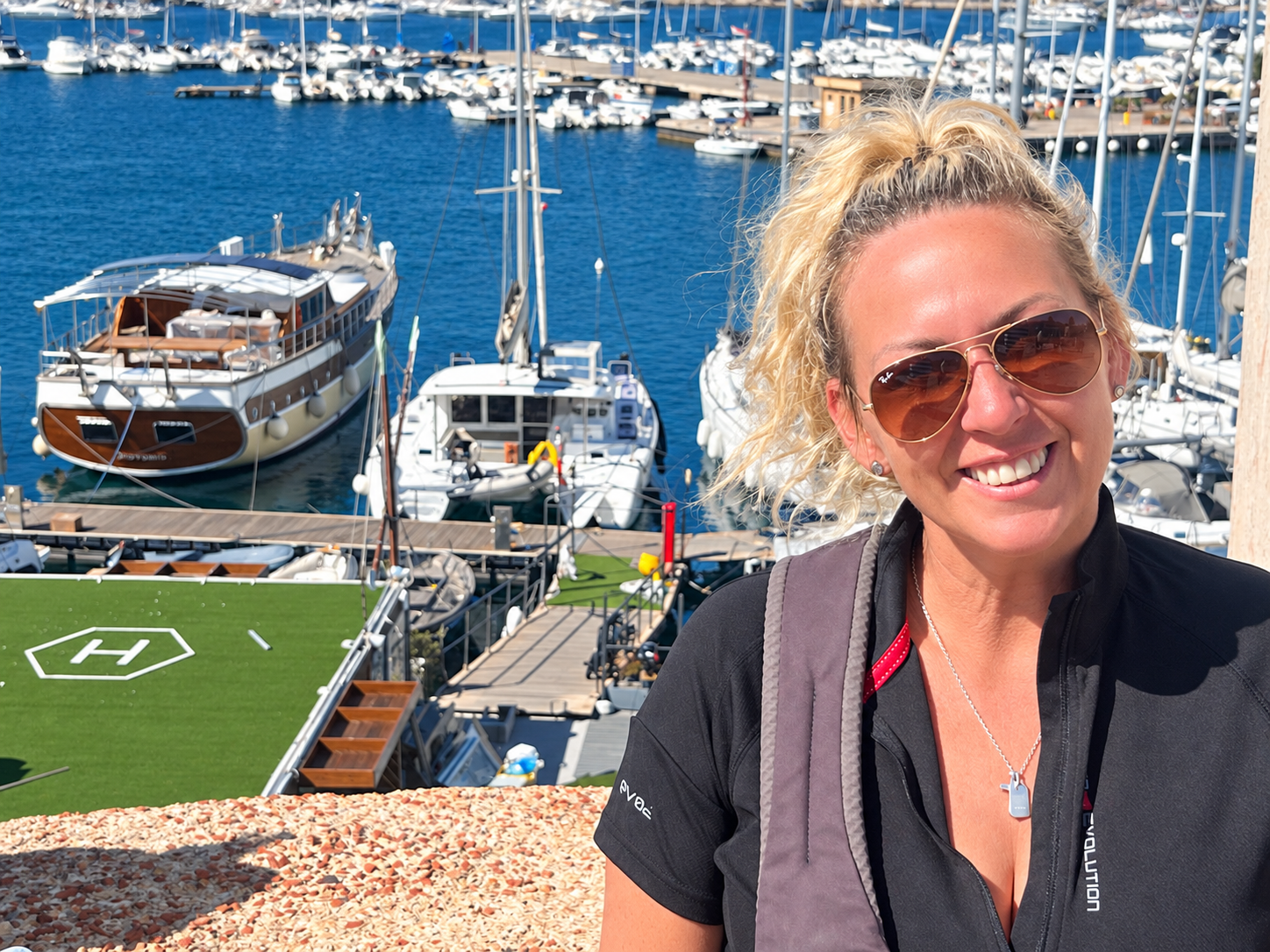 Rachel smiling above the marina, with RaRa moored below and behind her
